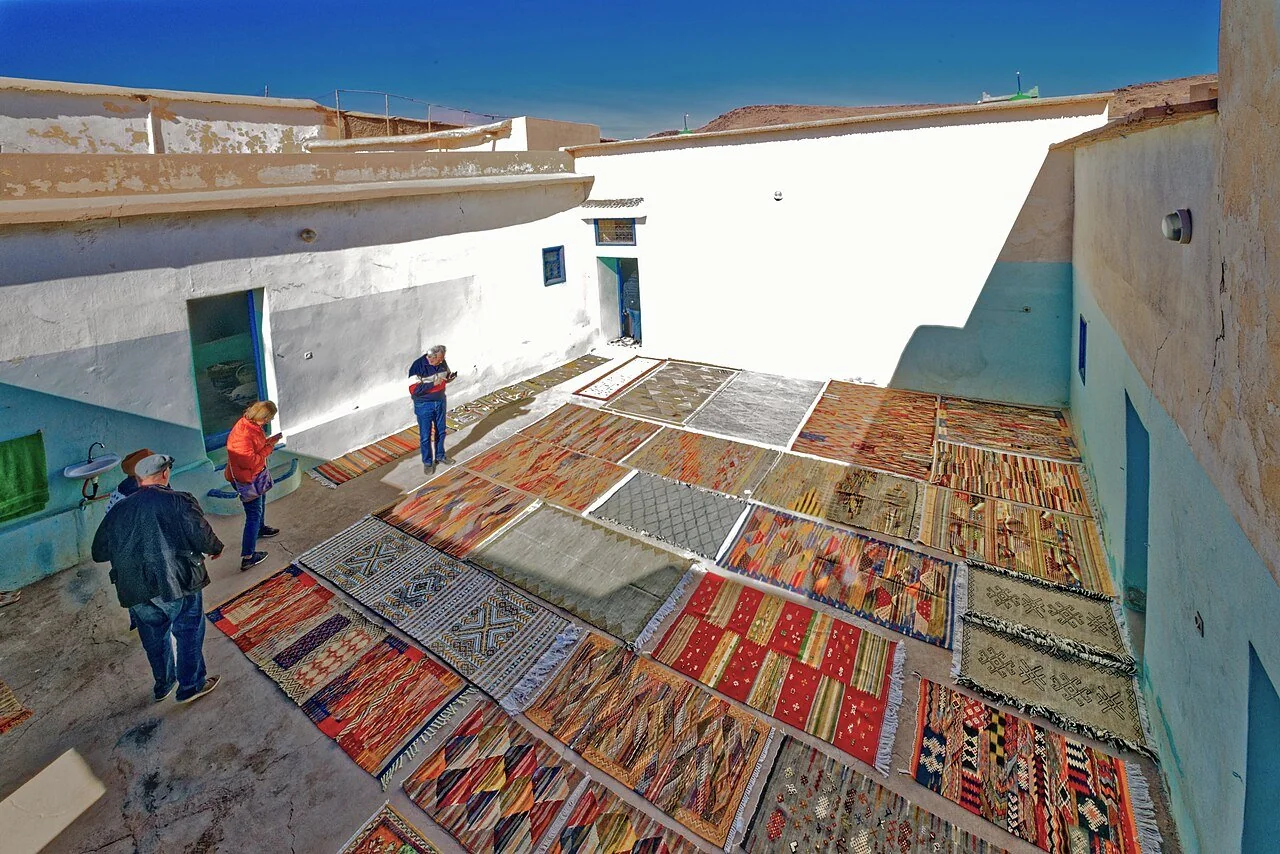Patterned carpets laid out across a sunlit courtyard at a Taznakht carpet workshop.