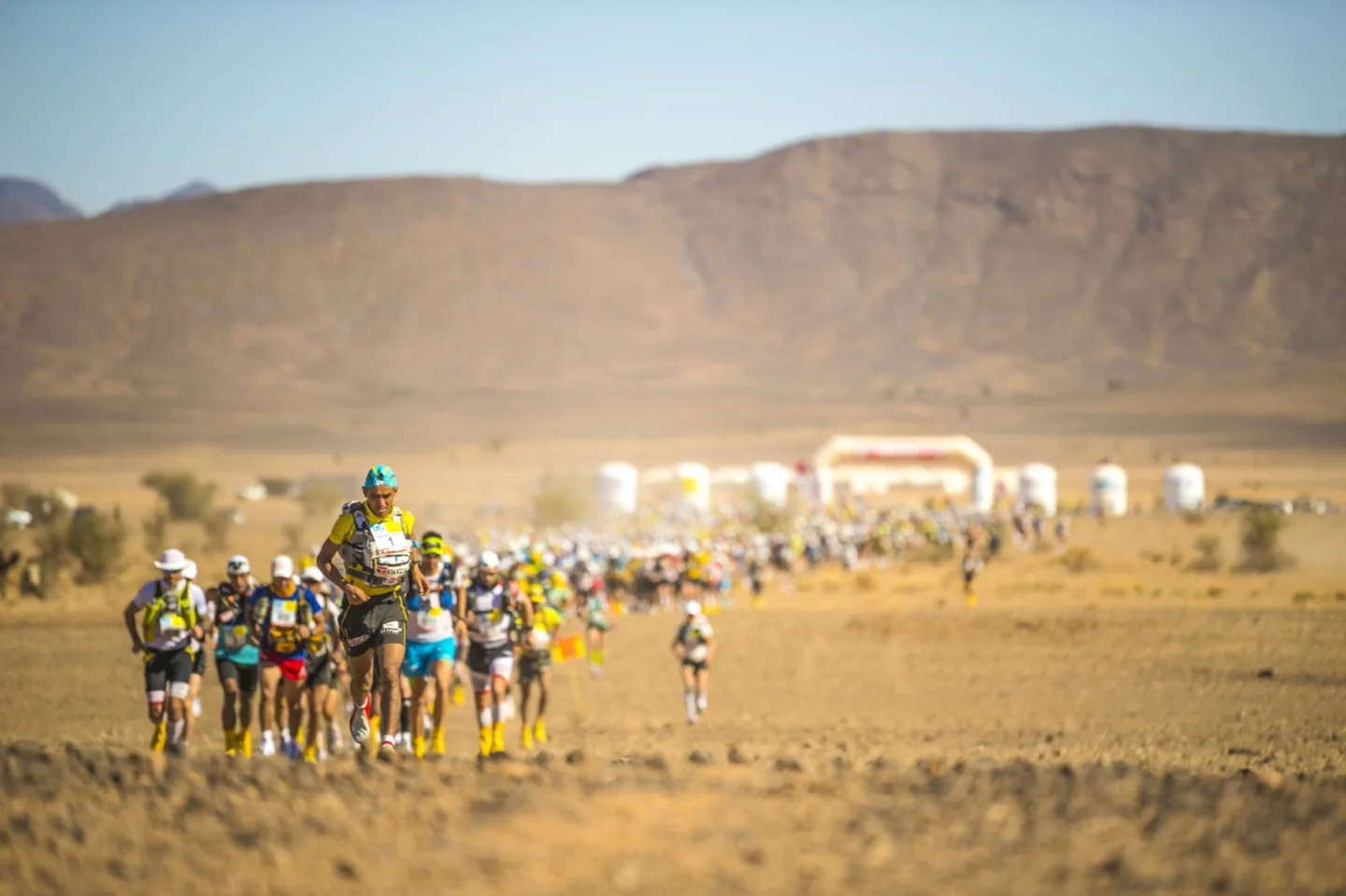 A pack of Marathon des Sables runners crossing an arid desert plain.