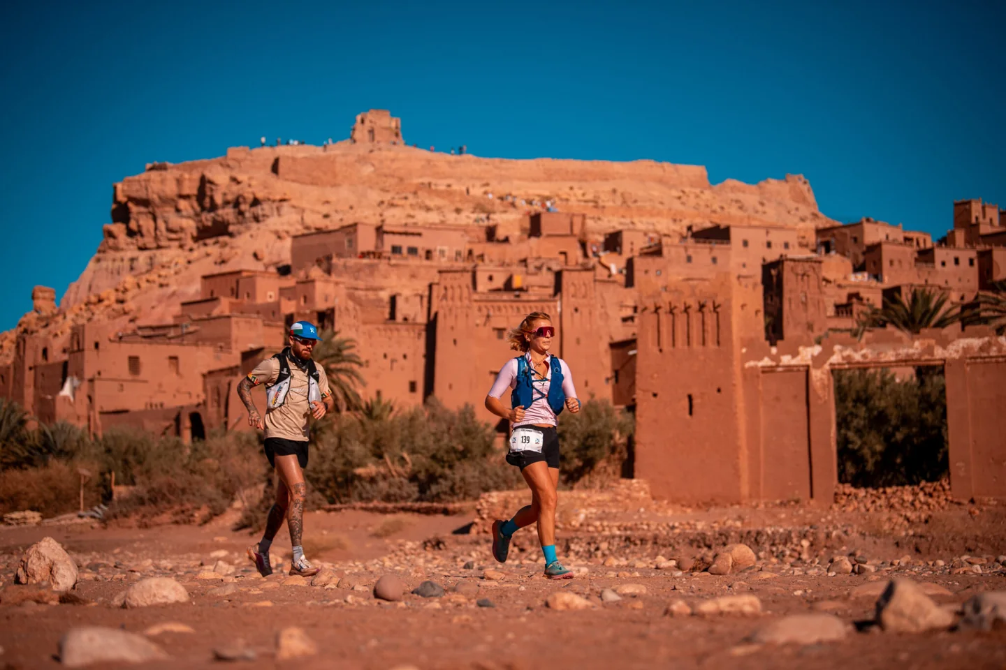 Ultra X Morocco competitors running past earthen kasbah buildings.